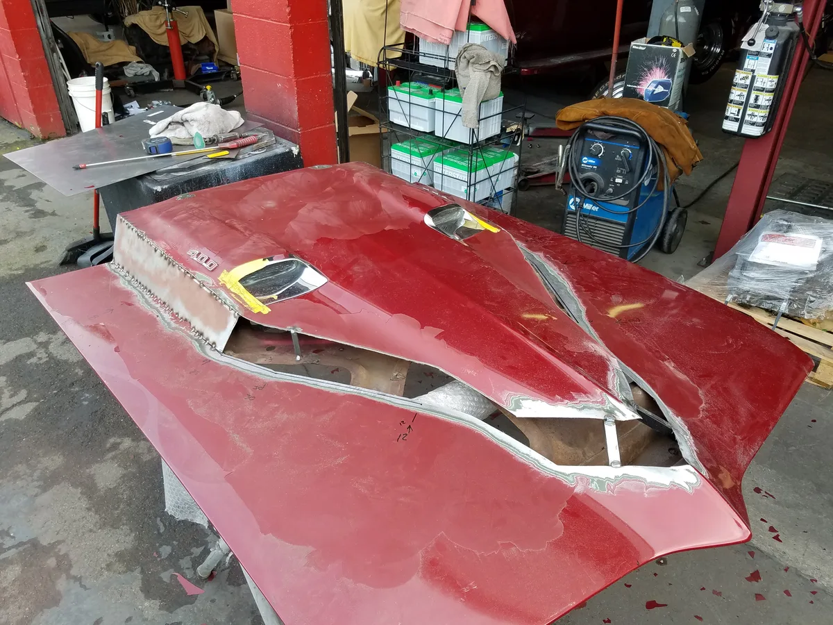 Damaged red hood panel with dents and rust on workbench